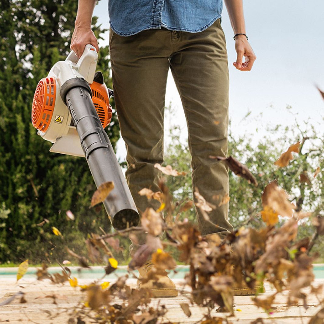 Person using STIHL BG56 blower for sale to clear dry leaves outdoors in a garden