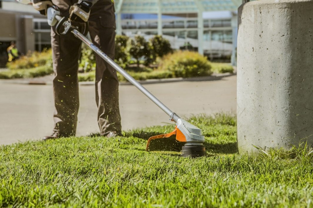 Person using STIHL FSA 90R brushcutter for sale to trim grass near a concrete post