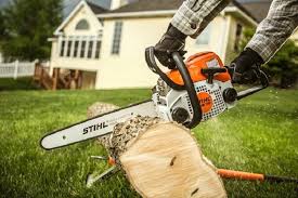 Stihl MS 210 chainsaw cutting through a log outdoors with a house in the background