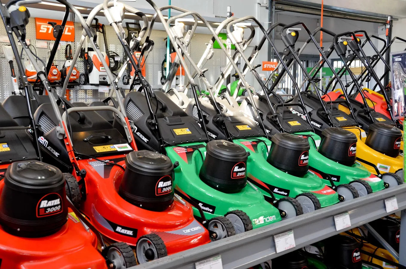 Row of various red and green lawnmowers for sale neatly displayed on store shelves