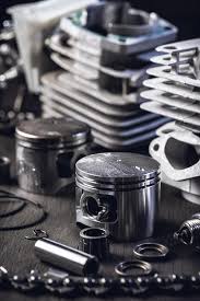 Close-up of various lawnmower spare parts including pistons, rings, and engine components on a workbench