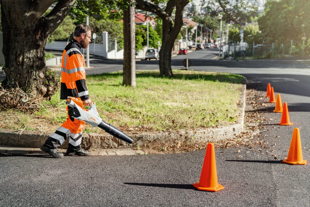 Man using STIHL BGA86 blower for sale to clear leaves along a sidewalk in a residential neighborhood