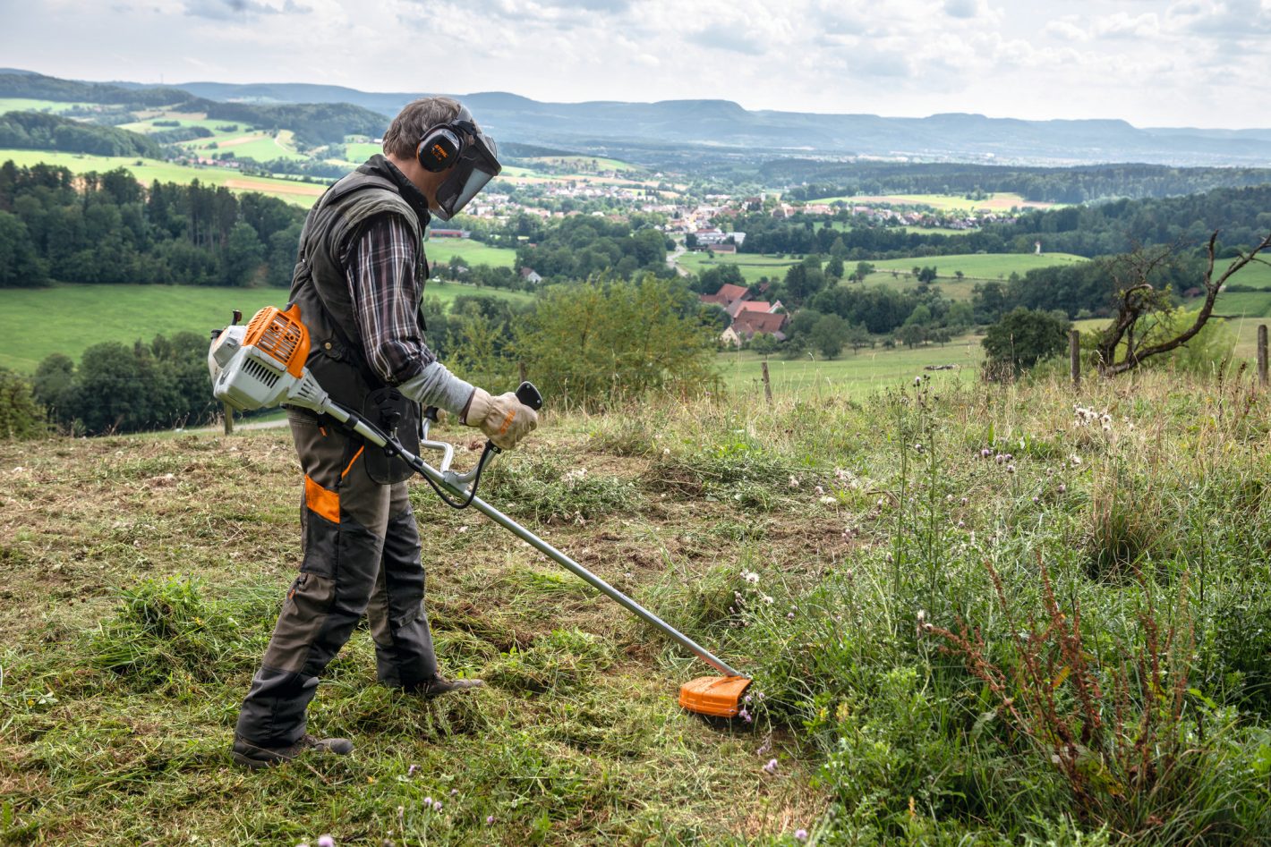 Man using STIHL FS 235 brushcutter for sale to clear thick grass and weeds in a rural field