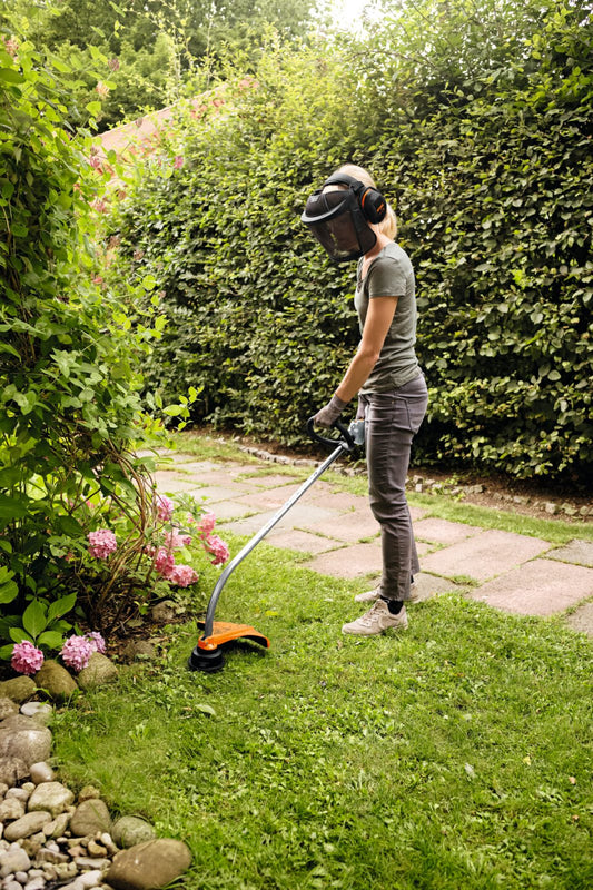 Person using FS 38 petrol grass trimmer to trim grass near garden path and flowers