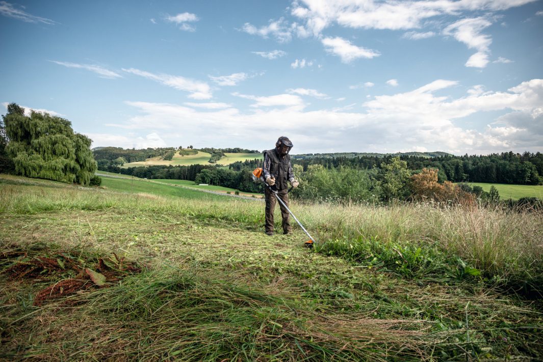 Person using STIHL FS230 brushcutter for sale to trim grass and weeds in a large open field