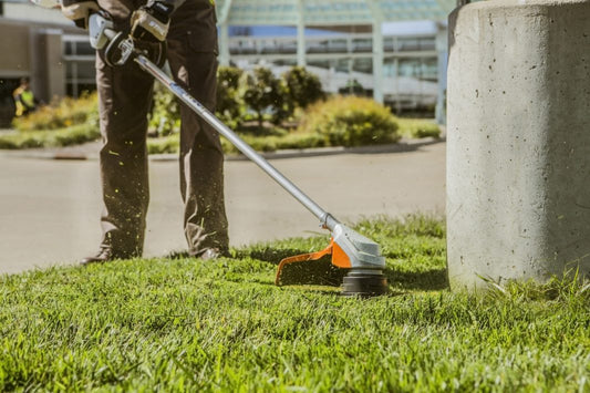 Person using STIHL FSA 90R brushcutter for sale to trim grass near a concrete post