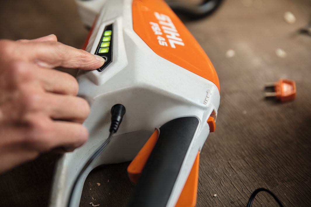 Close-up of hand pressing power button on orange and white STIHL FSA45 trimmer for sale battery indicator