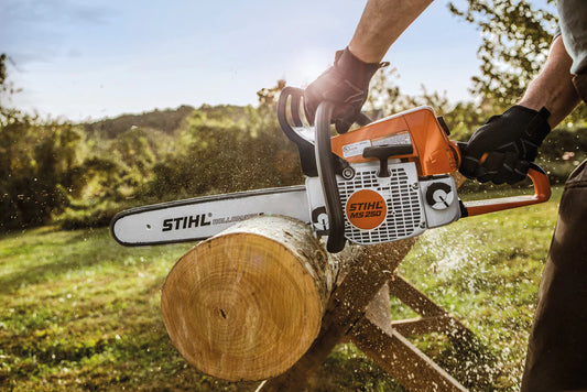 Person using Stihl MS250 chainsaw for sale to cut a log outdoors in a sunny forest setting